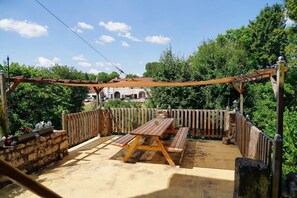 Un patio al aire libre con mesa y bancos de madera, rodeado por una valla de madera y muros de piedra.