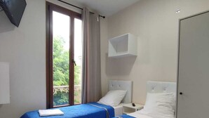 A hotel room with two beds, a TV mounted on the wall, and a window with curtains. - RENT APPART - La Garenne Colombes (La Garenne-Colombes)
