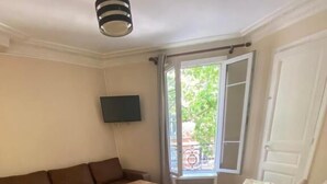 A room with a brown sofa, a white table, and a bed with a beige cover. - RENT APPART - La Garenne Colombes (La Garenne-Colombes)
