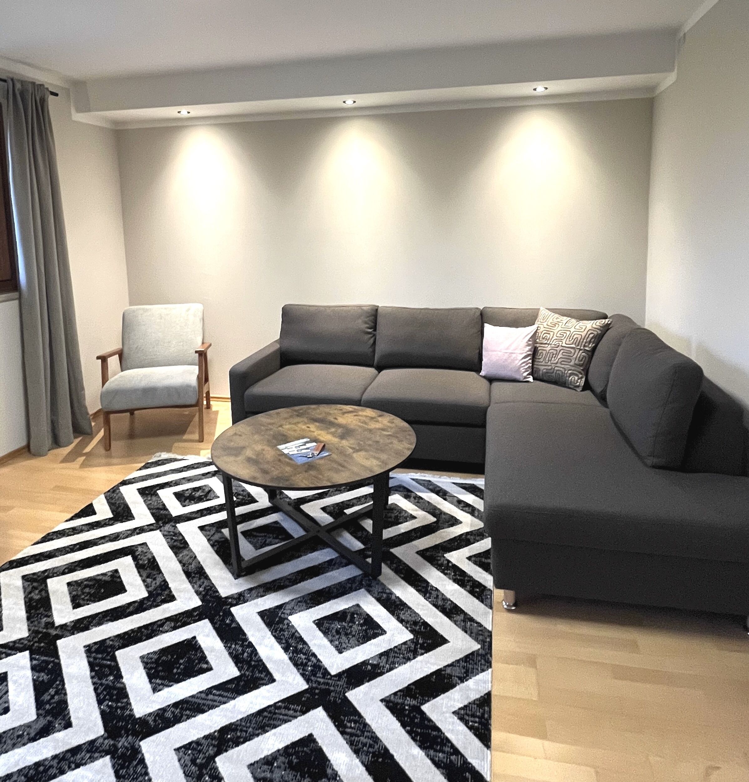A modern living room with a grey sectional sofa, a round coffee table, and a patterned rug.