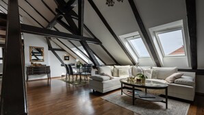 Un salon de style industriel, avec un plafond haut, des poutres apparentes, un canapé blanc, une table basse en verre et un coin repas comprenant une table et des chaises.