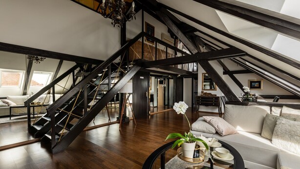 Un loft spacieux avec de hauts plafonds, des poutres apparentes, un escalier et un salon moderne comprenant un canapé et une table basse.