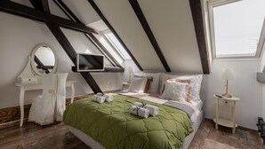 Une chambre avec un plafond en pente, un lit avec une literie verte, une table de chevet avec une lampe, une commode, un miroir et un téléviseur.