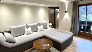 A modern living room with a grey sectional sofa, a round coffee table, and a large window with curtains. - FeWo Kampen - Wiefarn Apartments (Bad Wiessee)