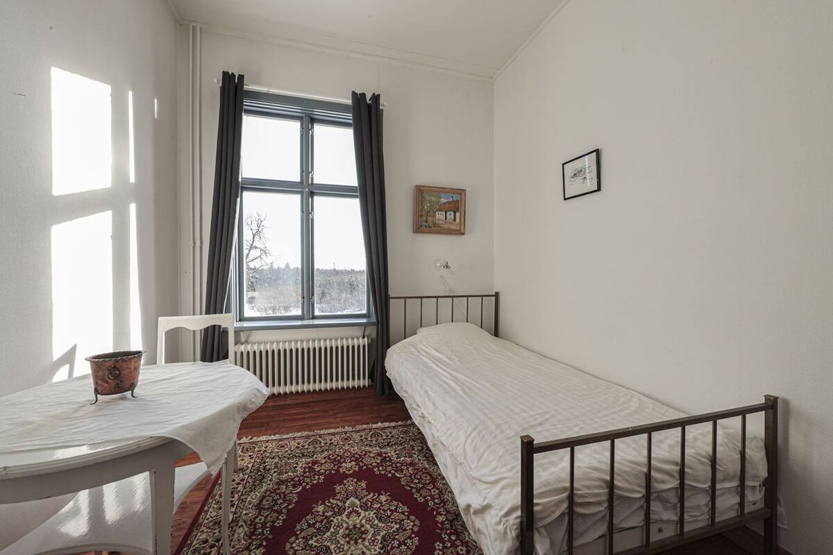A small, tidy room with a single bed, a table, a chair, and a radiator.