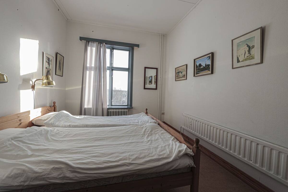 A room with two beds, a window with curtains, and several framed pictures on the wall.