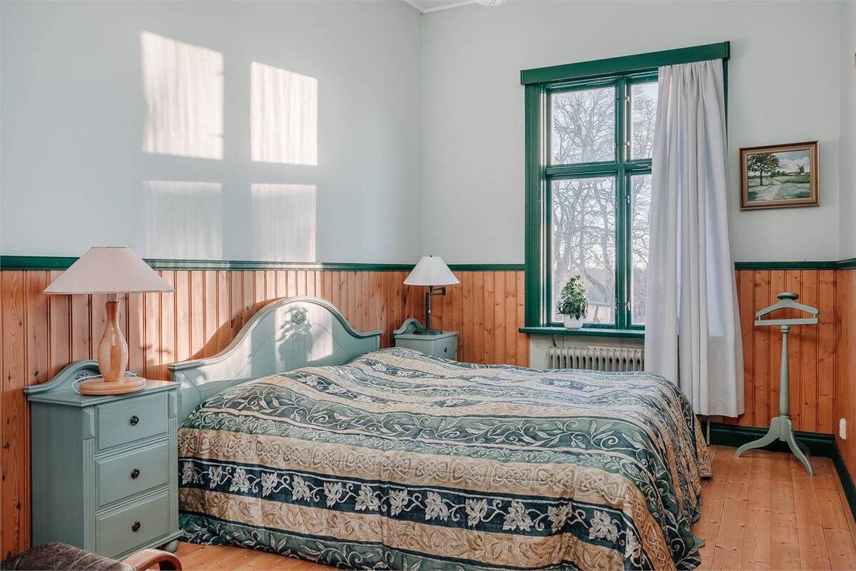 A bedroom with a bed, two bedside tables, a window with curtains, and a radiator.