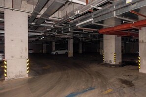 An underground parking garage with concrete pillars, a wet floor, and a white car parked in the distance. - West Hotel (Fengcheng)