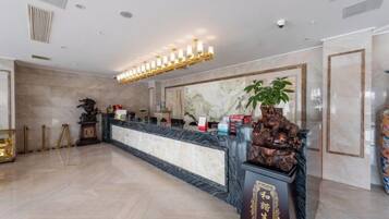 A hotel lobby with a marble reception desk, a large mirror, and a decorative plant.