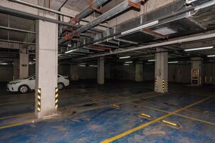 Un aparcamiento subterráneo con pilares de hormigón, líneas amarillas delimitando las plazas y un coche blanco estacionado en una de ellas.