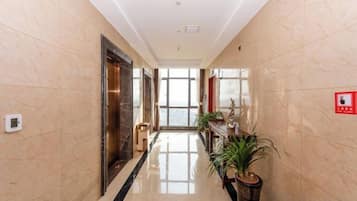 A hallway with a marble floor, a fire alarm on the wall, and a potted plant.