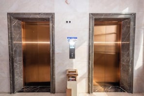 Two elevator doors with a sign above indicating the direction to the elevator. - West Hotel (Fengcheng)