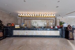 Una zona de recepción de hotel con mostrador de mármol, iluminación suspendida y un espejo grande.
