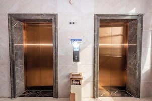 Dos puertas de ascensor frente a una pared de mármol y una pequeña señal encima.