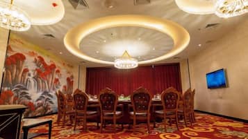 A conference room with a round table, chairs, a chandelier, a painting on the wall, and a television on the wall.