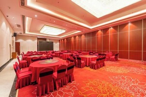Un salón de conferencias con varias mesas redondas, cada una rodeada de sillas, en una sala con alfombra roja y un amplio estampado floral.
