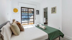 A bedroom with a bed, pillows, a green bedspread, a window with a view, and a door leading to a bathroom. - Sunny Duplex W/ Pool & Balcony by LovelyStay (Carvoeiro)