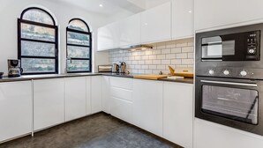 A modern kitchen with white cabinets, a double sink, a coffee maker, a kettle, a cutting board, and a stove. - Sunny Duplex W/ Pool & Balcony by LovelyStay (Carvoeiro)