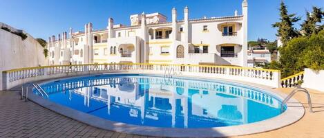 A swimming pool with a white fence and a building with balconies in the background.