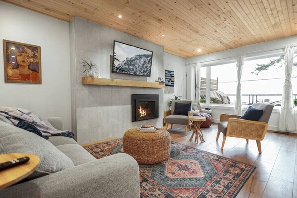 Un salon chaleureux avec une cheminée, des fauteuils confortables et une grande fenêtre donnant sur un beau paysage.
