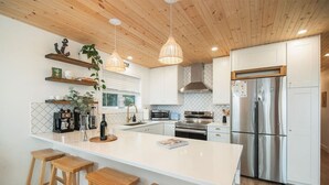 A modern kitchen with a central island, wooden stools, stainless steel appliances, and pendant lighting. - Sea, Sunrises, Sauna | Oceanfront Group Retreat (Campbell River)