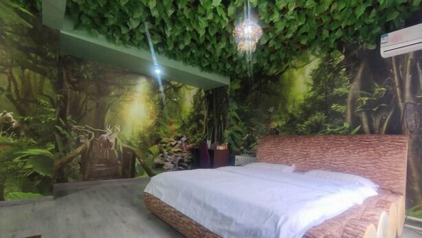 Une chambre à coucher avec un lit, une fresque murale représentant une forêt et un lustre suspendu.
