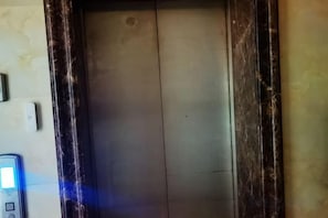 Intérieur d’un ascenseur avec une porte métallique et un panneau de commande situé à gauche.