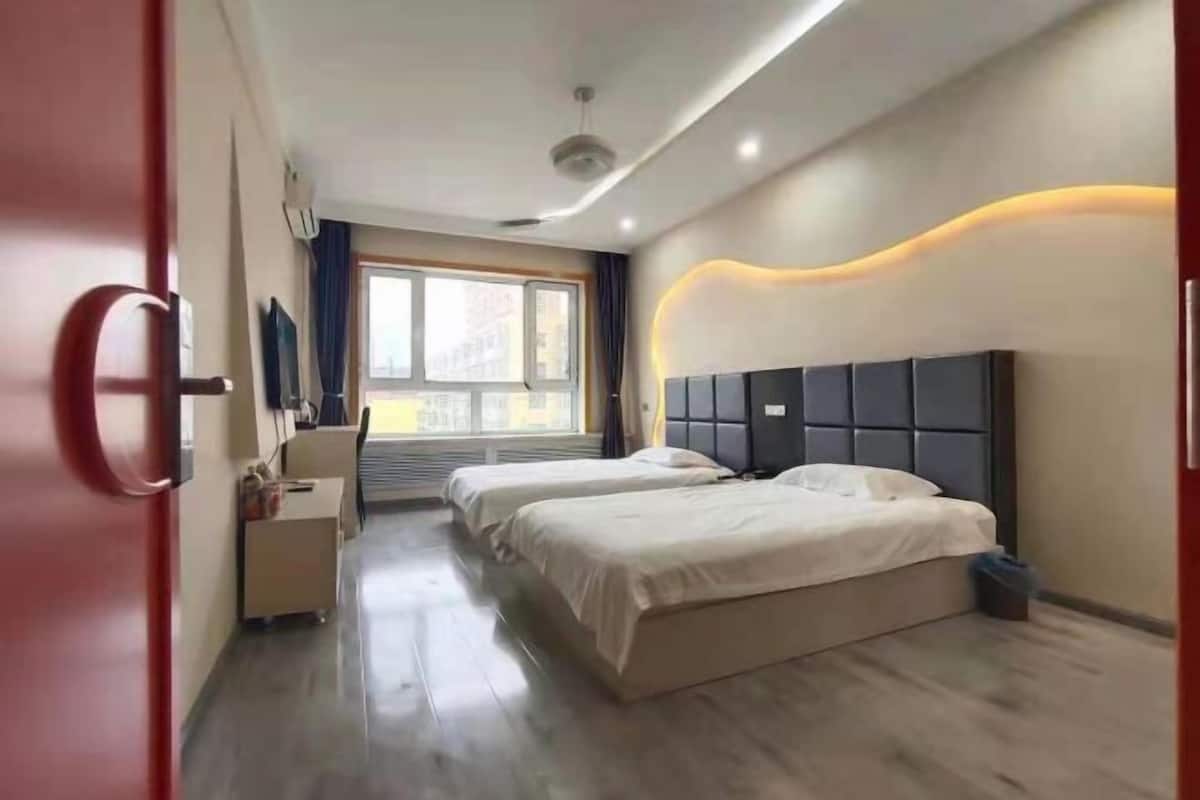 A modern hotel room with two beds, a desk, and a large window.