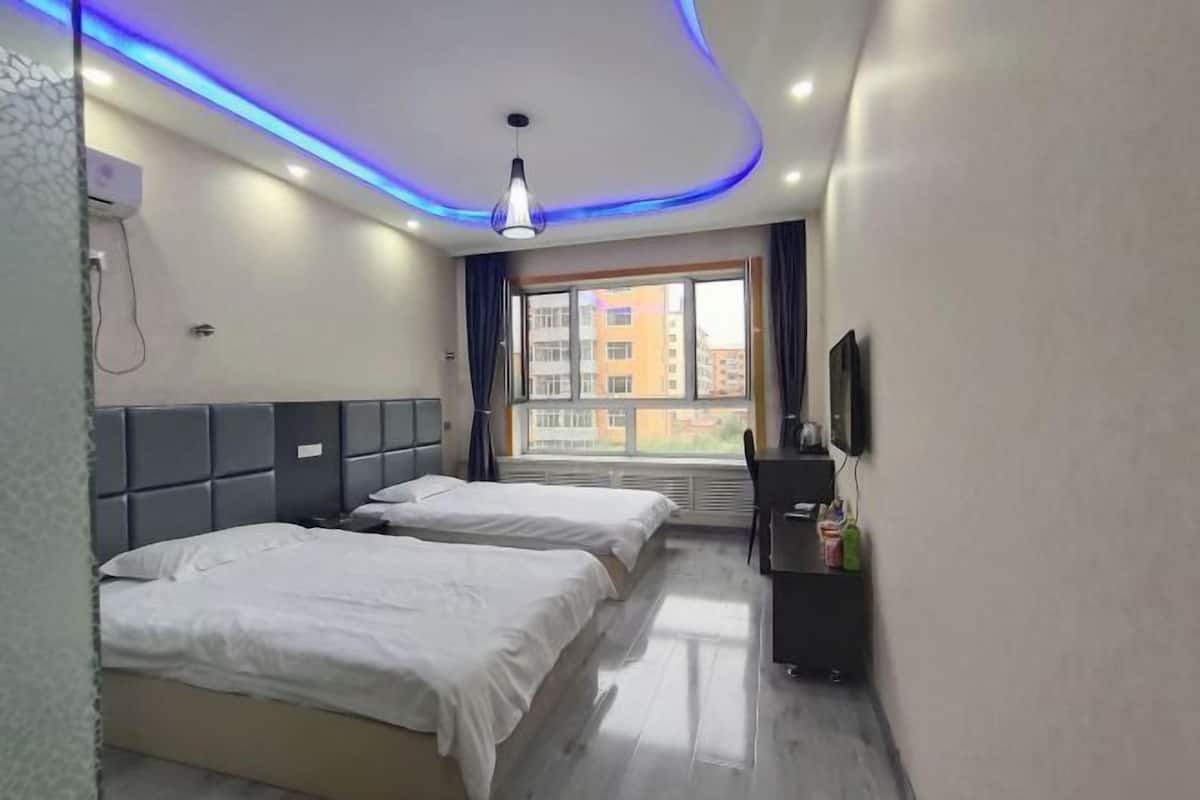 A hotel room with two beds, a TV, a desk, and a window with a city view.