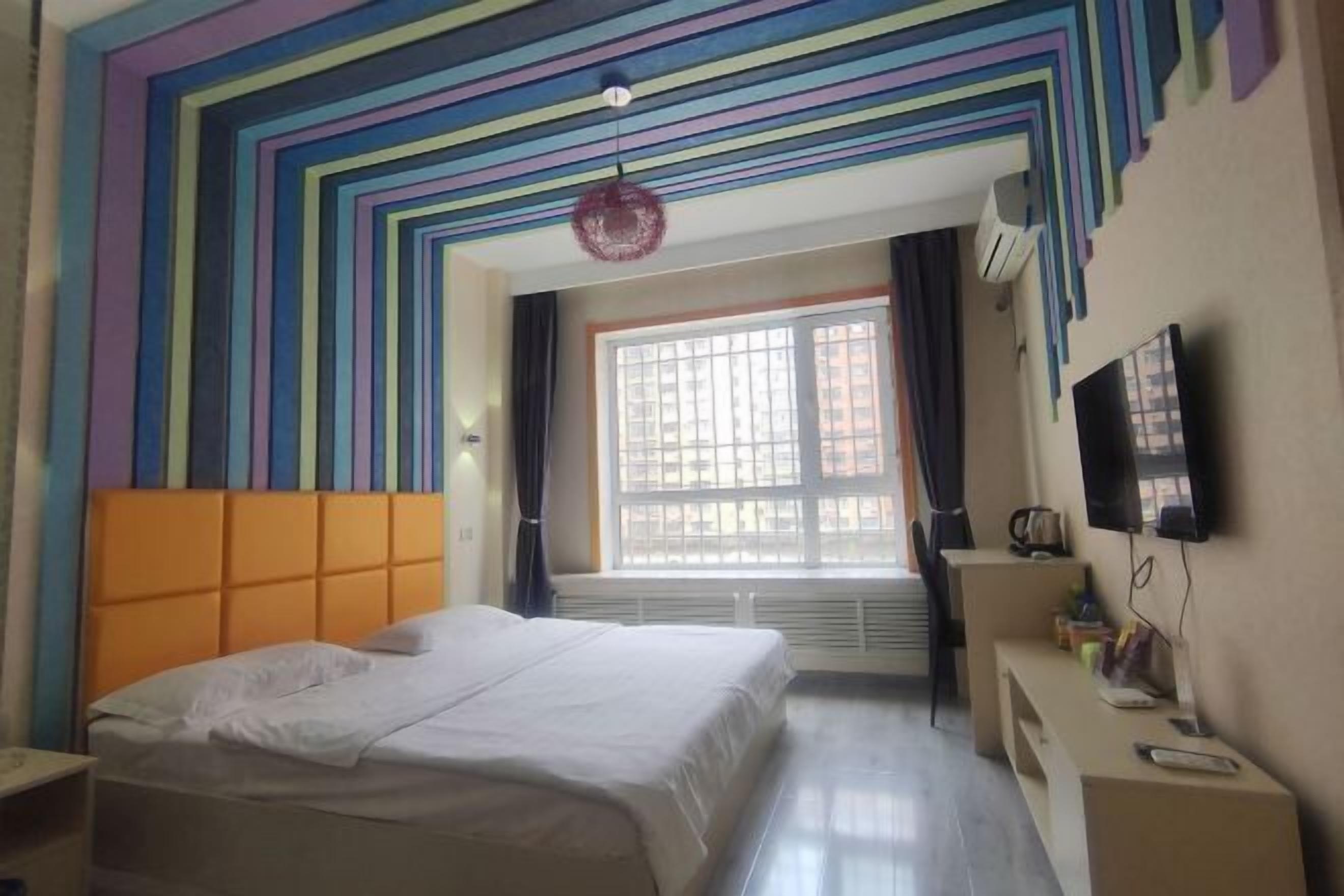 A hotel room with a bed, a TV, a desk, and a window with curtains.