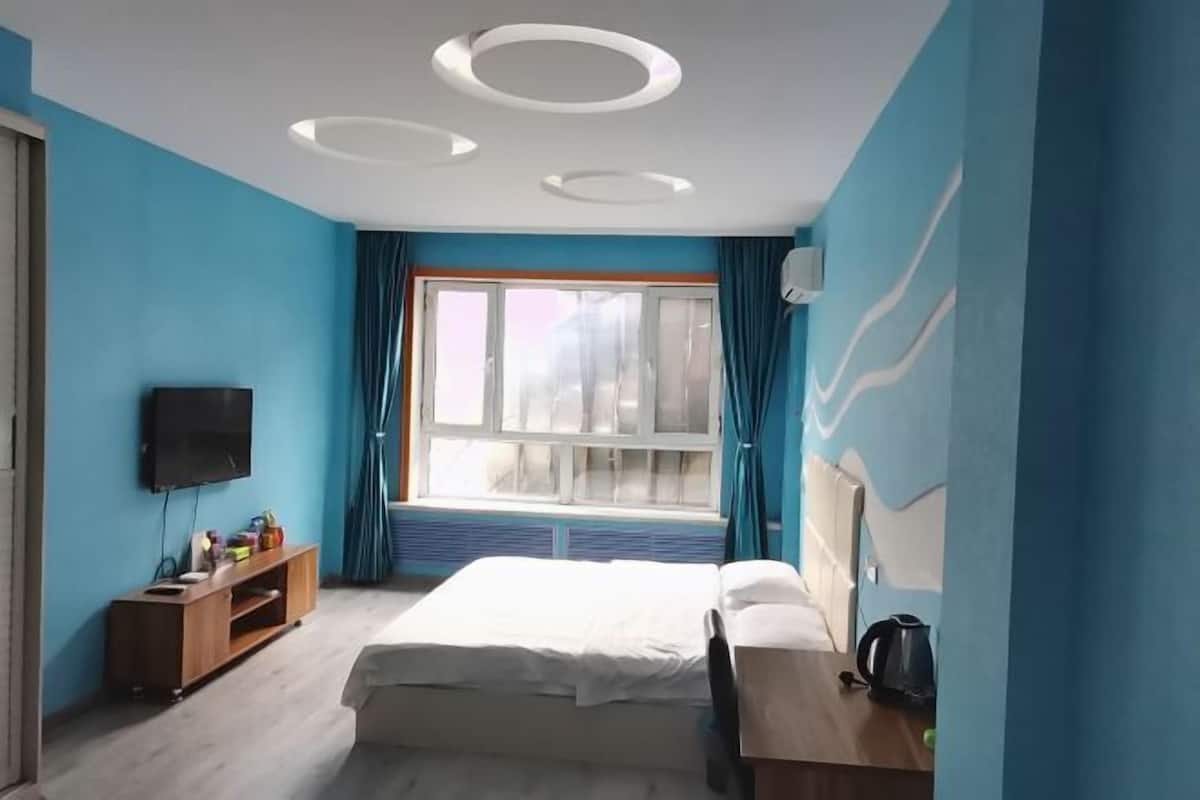 A modern hotel room with a large bed, a TV, a wooden side table, and a window with curtains.