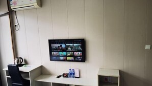 Une pièce équipée d’un téléviseur fixé au mur, d’un bureau avec une chaise et d’une étagère sur laquelle se trouvent une bouilloire et des bouteilles.