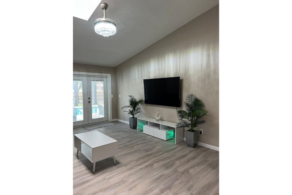 Un salon moderne avec un téléviseur à écran plat, une table basse blanche et deux plantes en pot.