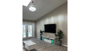 Una sala de estar moderna con un televisor de pantalla plana, una mesa de centro blanca y dos plantas en macetas.