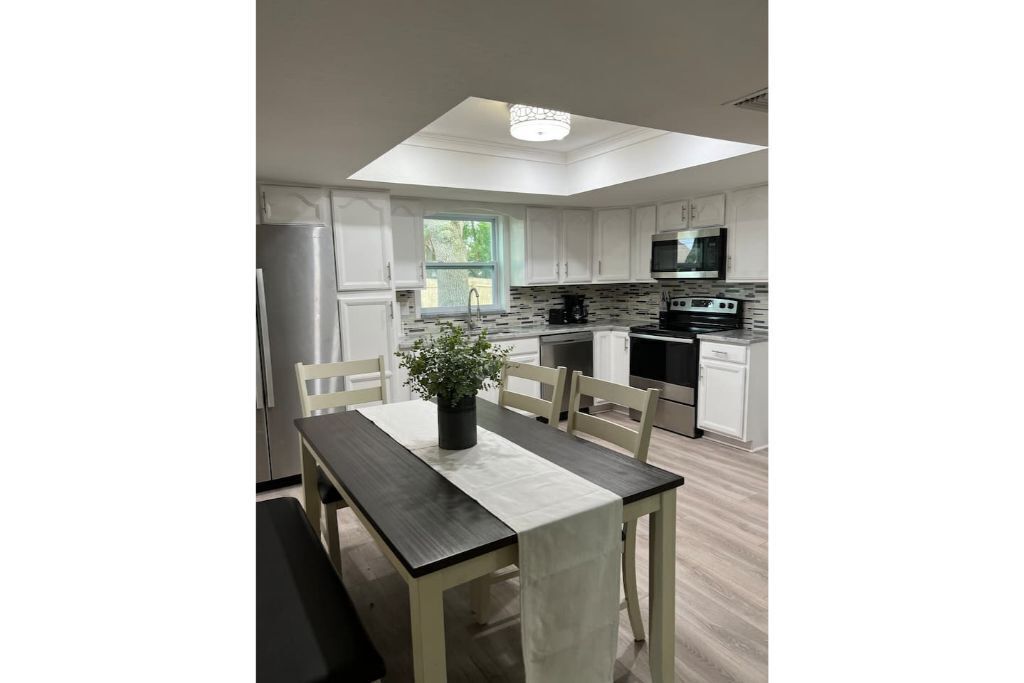 Una cocina moderna con armarios blancos, una isla central y un comedor con mesa y sillas.