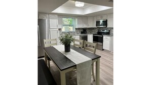Una cocina moderna con armarios blancos, una isla central y un comedor con mesa y sillas.
