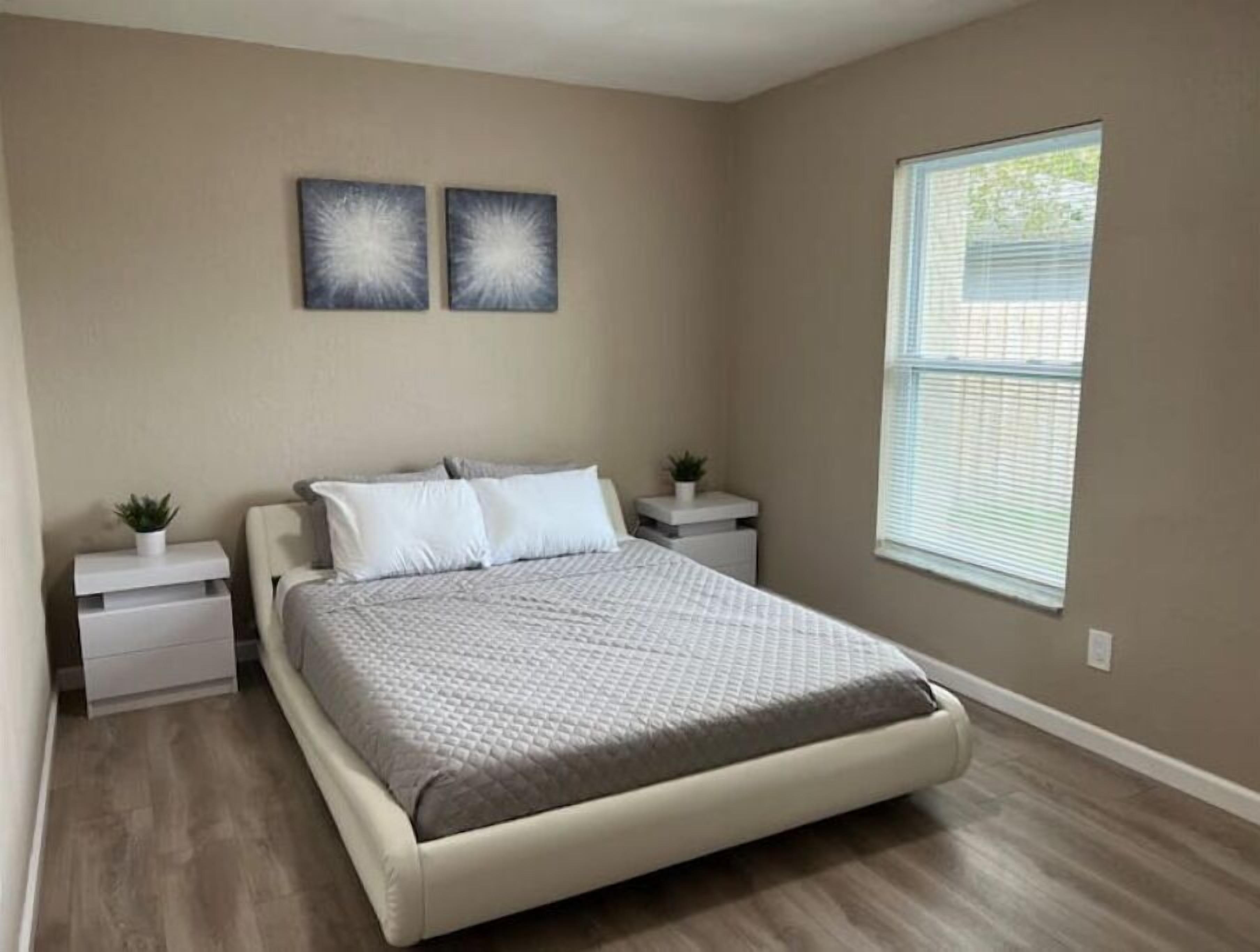 A bedroom with a bed, two nightstands, a window, and two wall art pieces.