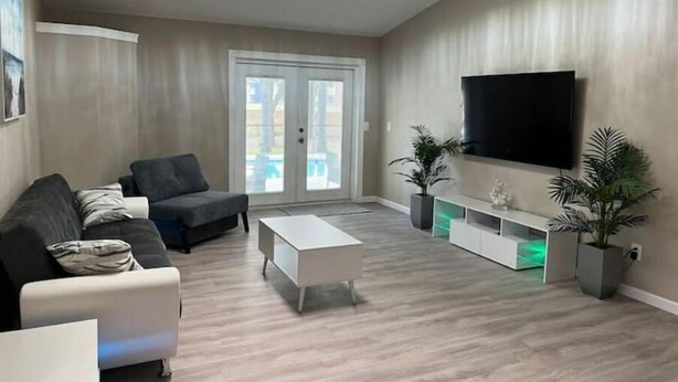 Una sala de estar moderna con un sofá gris, una mesa de centro blanca y un televisor montado en la pared.
