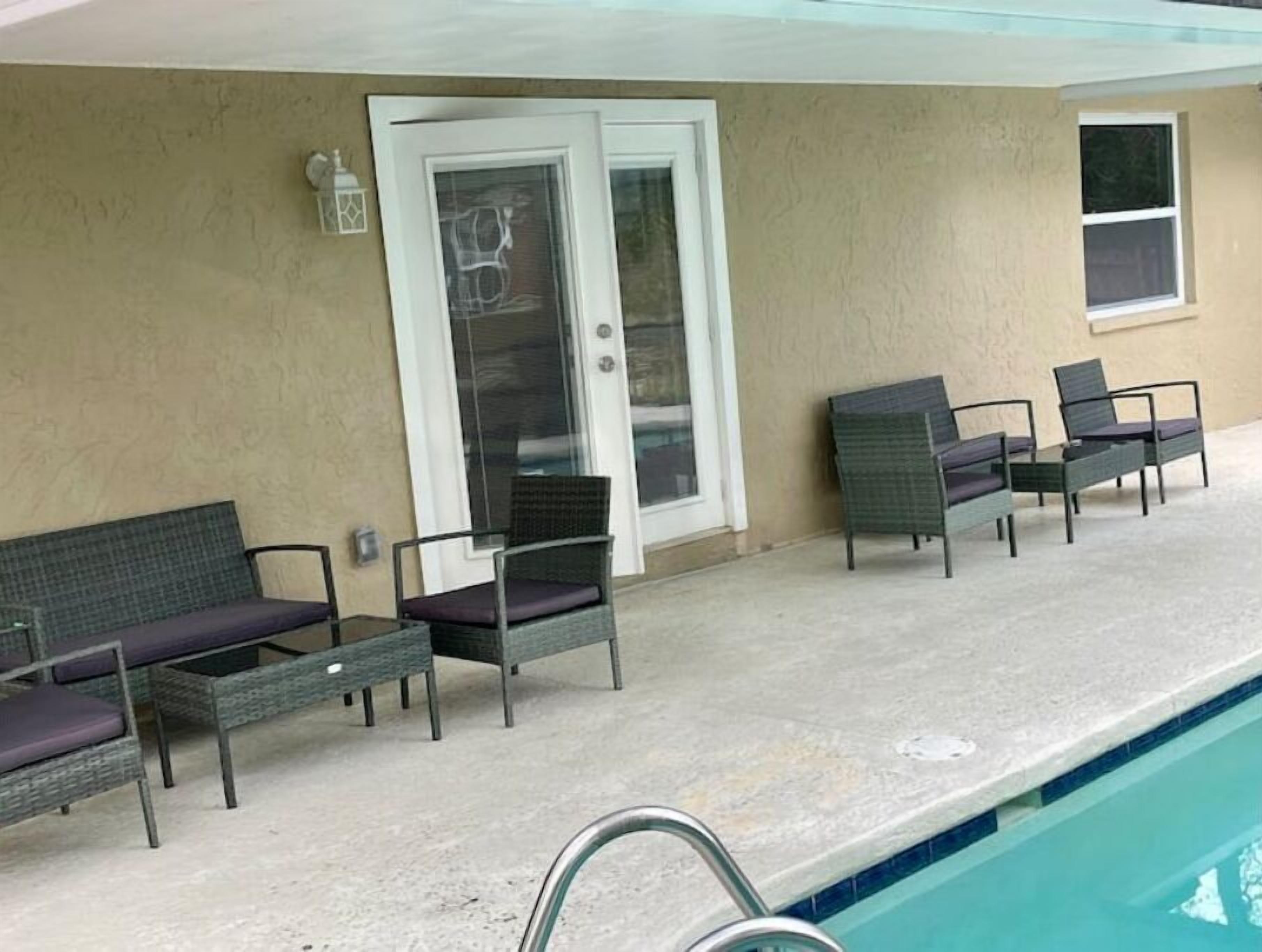 Zona de piscina con sillones de mimbre y puerta de vidrio que da a la piscina.