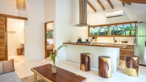A modern kitchen with wooden beams, a central island, and a large window overlooking greenery. - Unique beach side villa Rocamar Santa Teresa (Puntarenas Province)