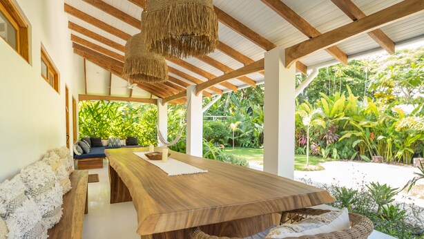 A covered outdoor dining area with a wooden table and benches, surrounded by lush greenery and a view of a garden. - Unique beach side villa Rocamar Santa Teresa (Puntarenas Province)