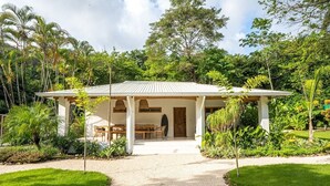 A bungalow with a covered patio, surrounded by lush greenery and a gravel path leading to the entrance. - Unique beach side villa Rocamar Santa Teresa (Puntarenas Province)