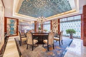 A dining area with a round table, chairs, a chandelier, and a patterned ceiling. - Xiliang Hotel (Wuwei)
