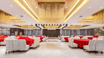 Un salón de banquetes con filas de mesas y sillas, un escenario y una araña.