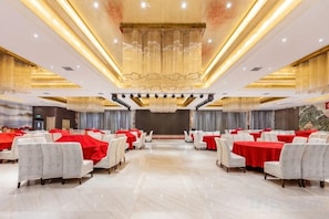 Un salón de banquetes con filas de mesas y sillas, un escenario y una araña.