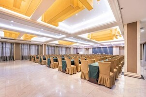 Un amplio salón de conferencias con filas de sillas y mesas, techos altos y modernas lámparas.