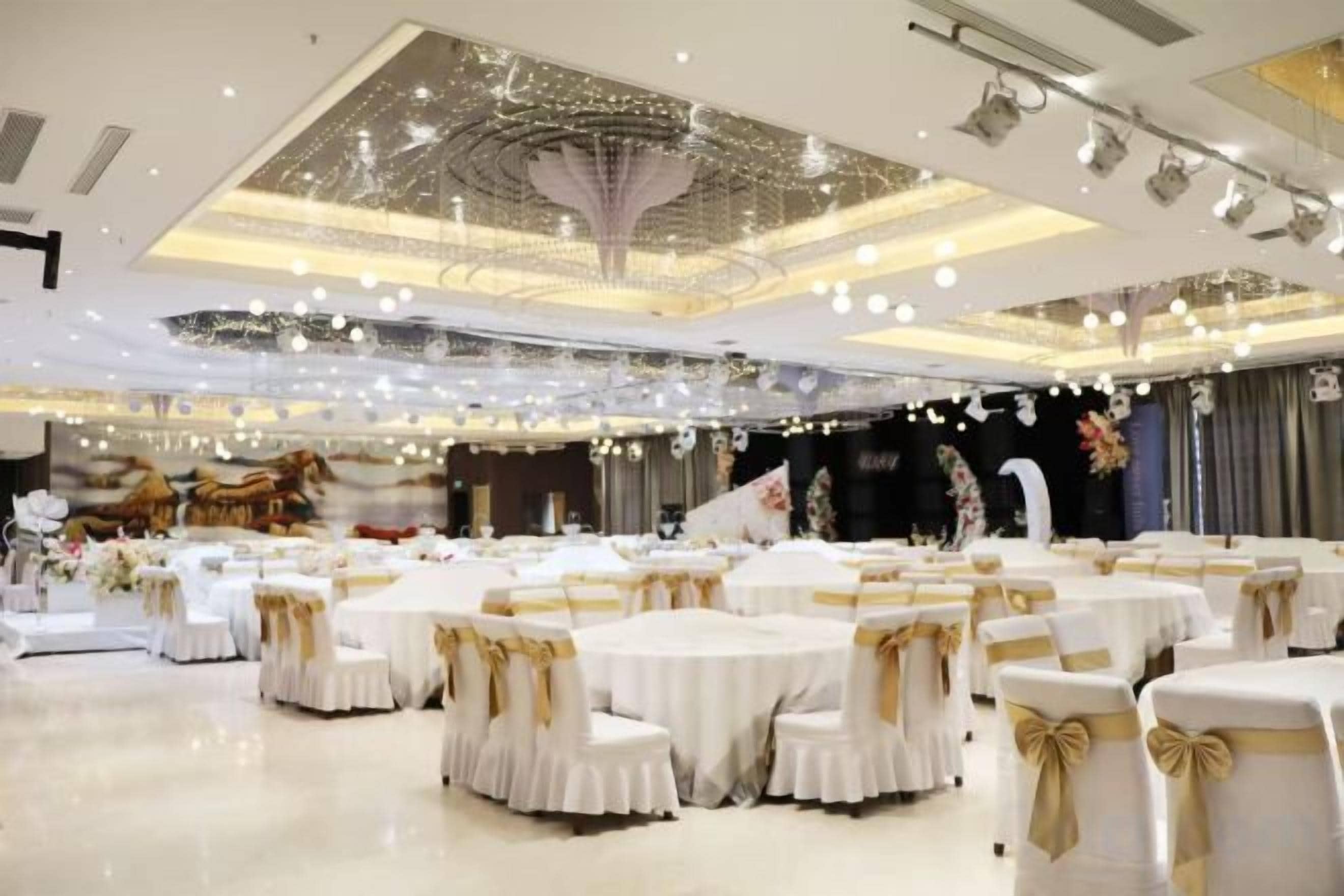 Une salle de banquet avec des tables rondes, des nappes blanches et des rubans dorés.