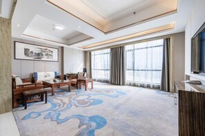 A spacious living area with a large window, a flat-screen TV, and a patterned carpet. - Xiliang Hotel (Wuwei)