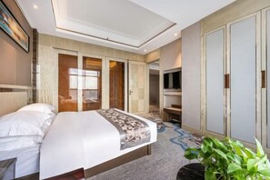 A hotel room with a bed, a TV, a wardrobe, and a plant. - Xiliang Hotel (Wuwei)