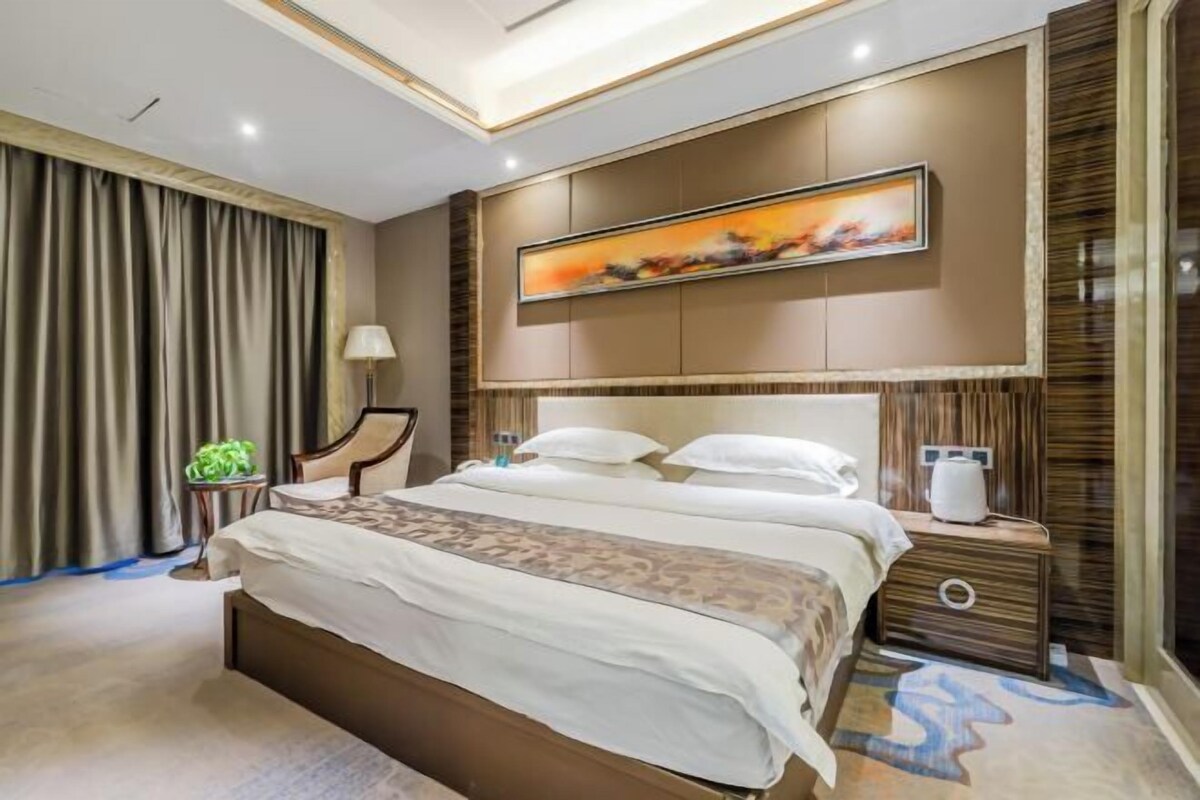 A hotel room with a large bed, a bedside table, a lamp, and a painting on the wall.